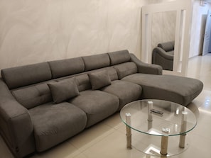 A grey sofa with a glass coffee table in a modern room with a tiled floor.