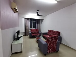 A living room with a flat-screen TV, a coffee table, two sofas, a ceiling fan, and a window with curtains.