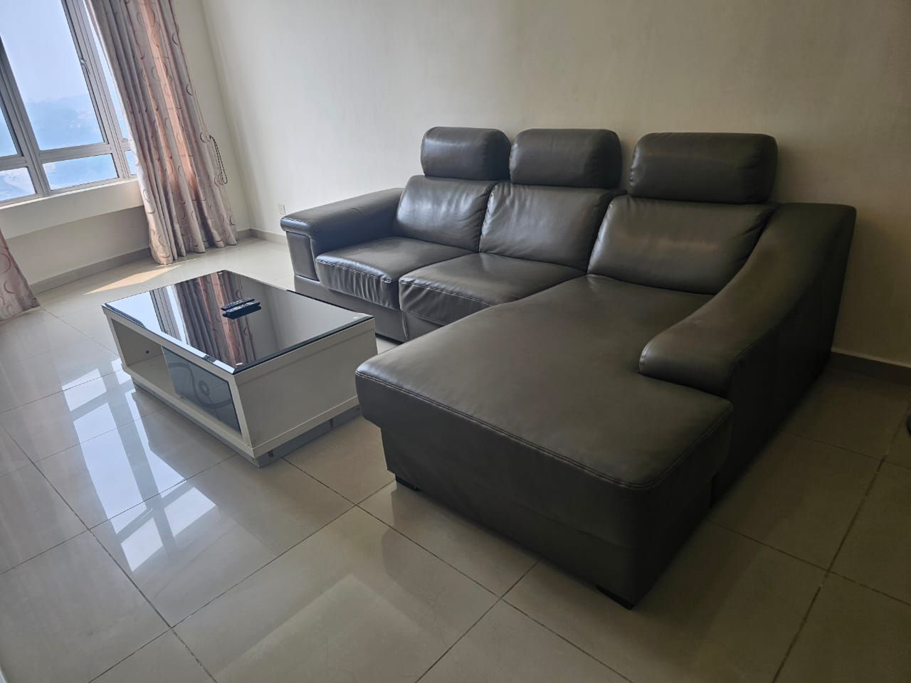 A modern living room with a sectional sofa, a glass coffee table, and a view of the outdoors through a window.