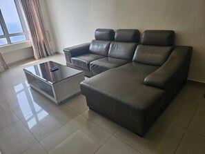 A modern living room with a sectional sofa, a glass coffee table, and a view of the outdoors through a window. - Putra Majestik (Kuala Lumpur)