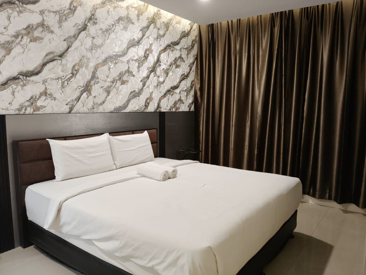 A hotel room with a large bed, a marble-patterned wall, and a curtain.