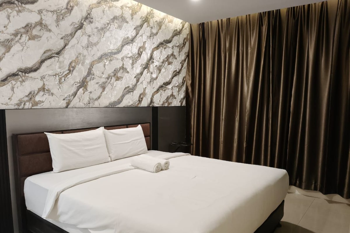 A hotel room with a large bed, a marble-patterned wall, and a curtain.