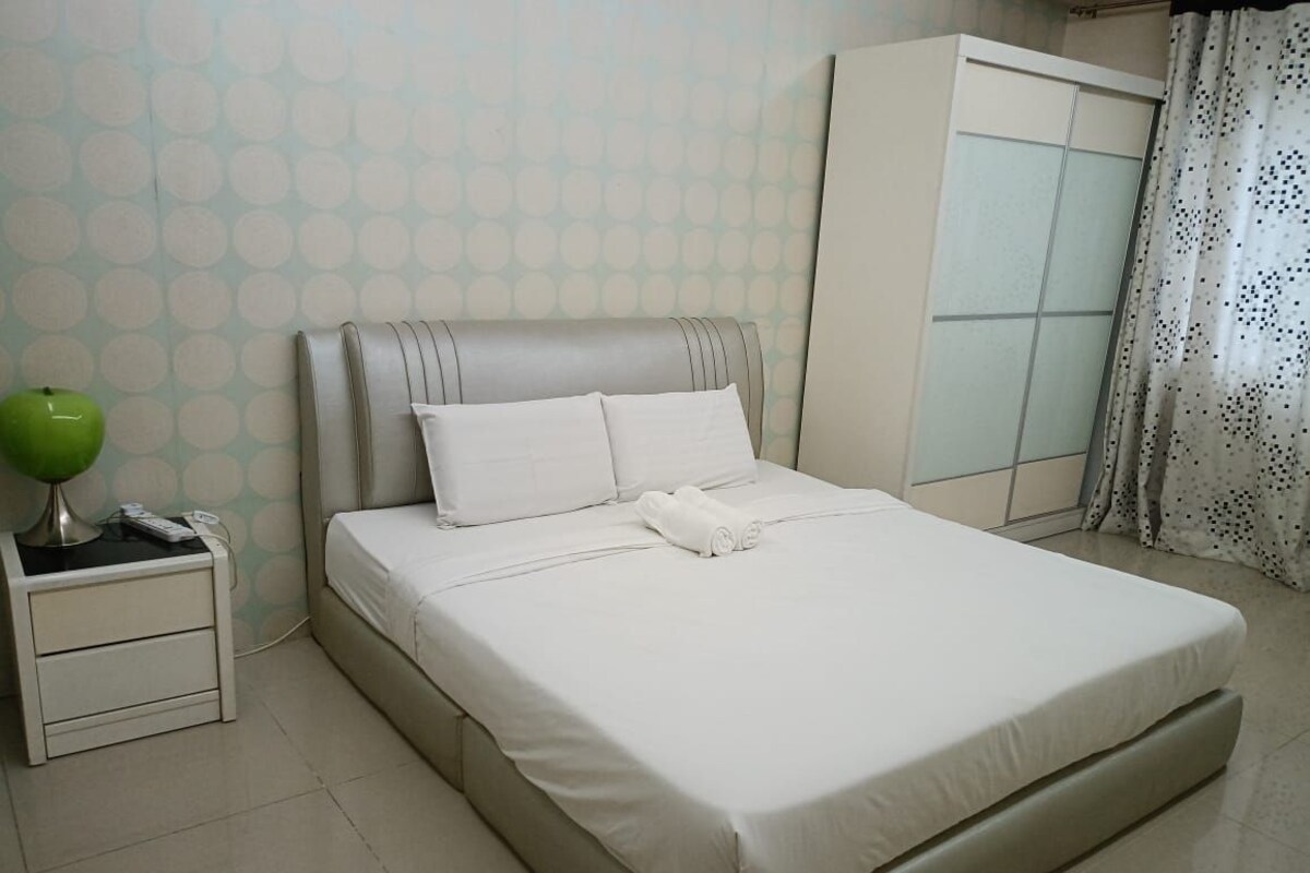 A neatly made bed with white bedding, a bedside lamp, and a wardrobe with a frosted glass door.