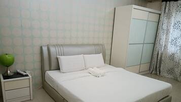 A neatly made bed with white bedding, a bedside lamp, and a wardrobe with a frosted glass door.