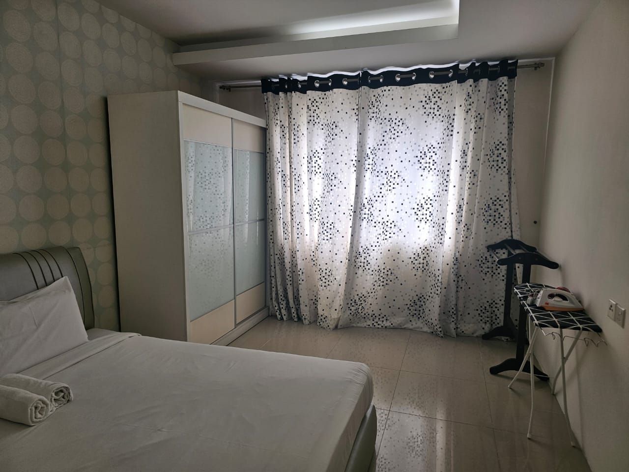 Ein Schlafzimmer mit einem Bett, einem Kleiderschrank, einem Vorhang und einem Bügelbrett.