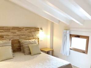 A bedroom with a stone headboard, a bedside table, and a window with curtains. - Sogno Azzurro - Quadrilocale Deluxe 17 (Porto Azzurro)