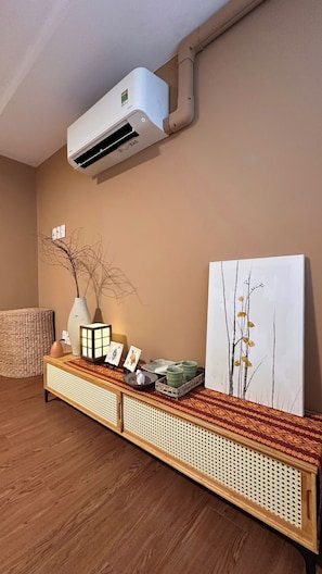 Ein Zimmer mit Wandklimaanlage, einer gewebten Rattanbank und einem gerahmten Gemälde.