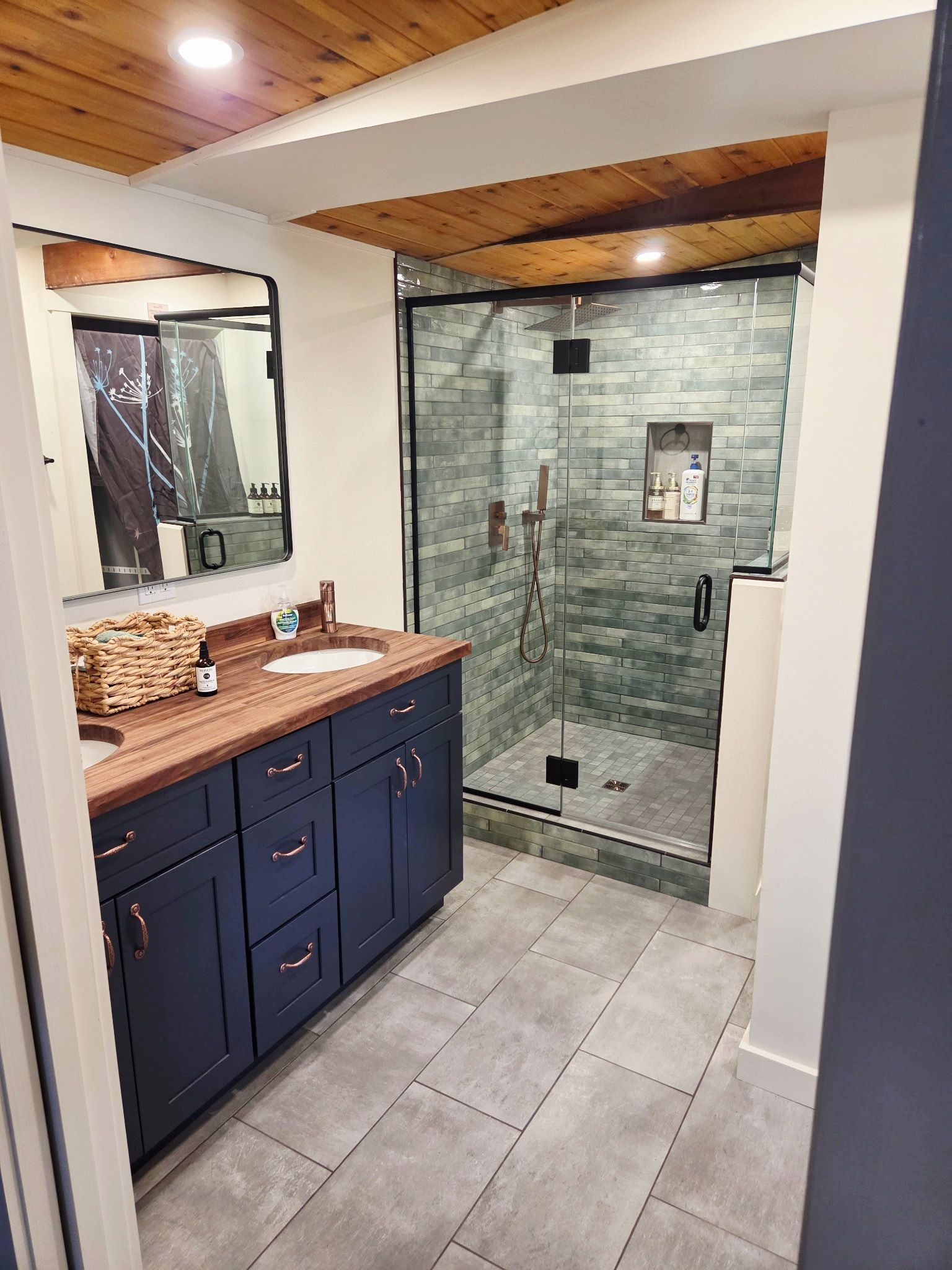 Un bagno con soffitto in legno, cabina doccia in vetro, lavabo con specchio e mobili scuri.