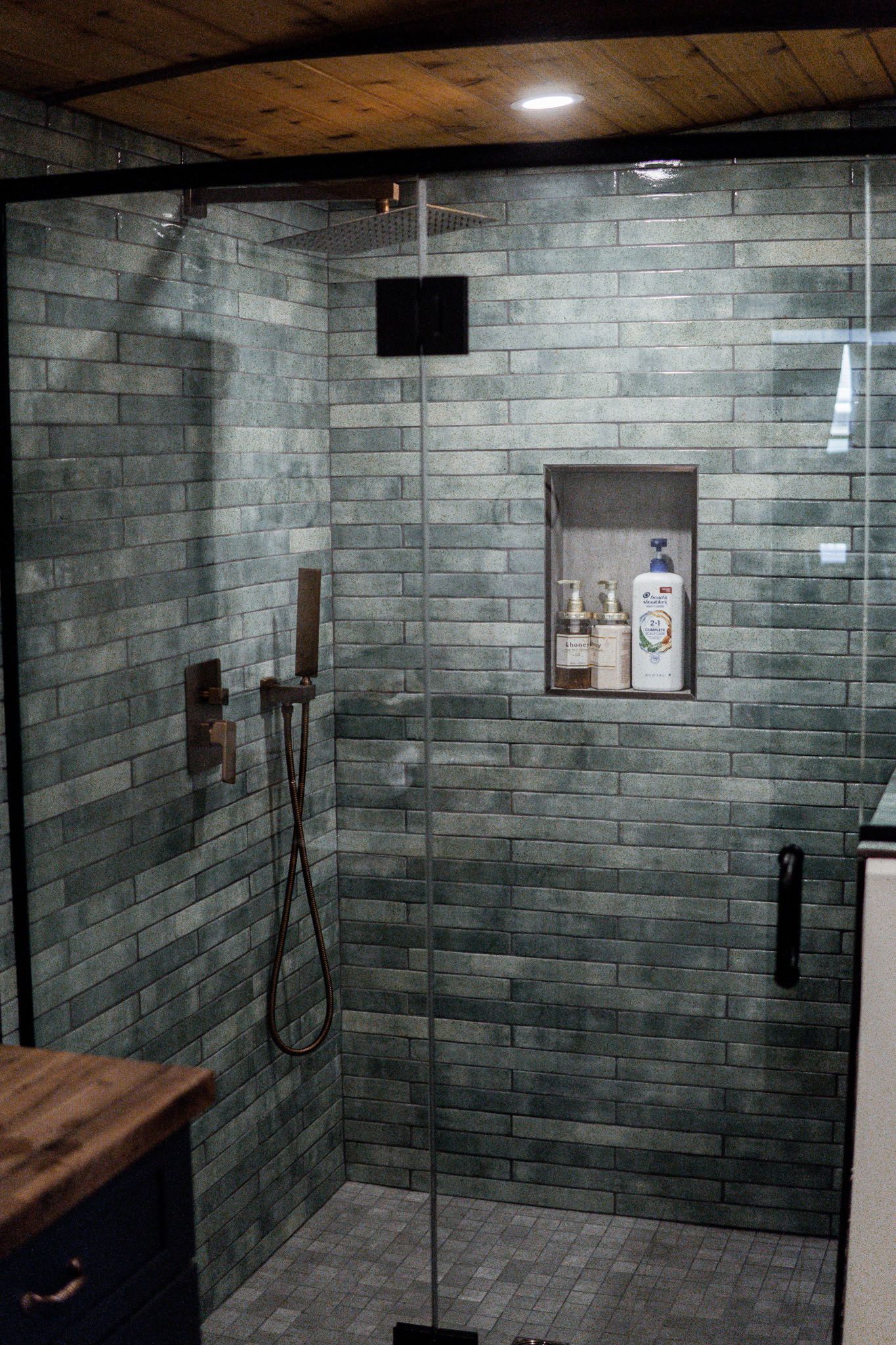 A shower area with a glass door, a wooden bench, and a shelf with toiletries.