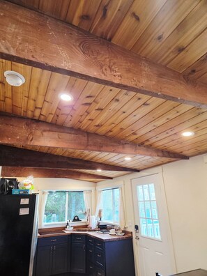 A kitchen with wooden ceiling beams, a black refrigerator, and a window with curtains.
