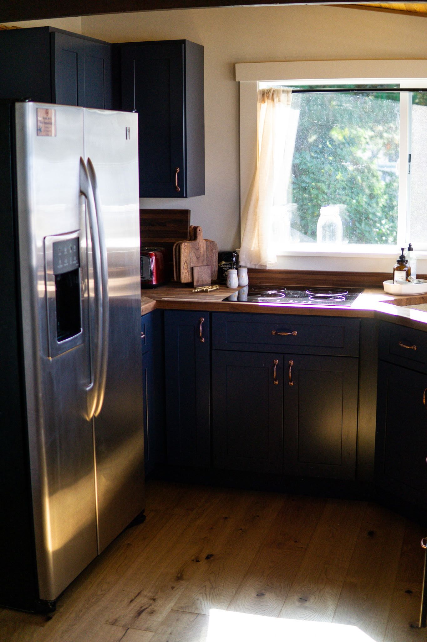 Una cocina con un refrigerador de acero inoxidable, gabinetes oscuros, una encimera de madera y un ventanal con vistas a zonas verdes.