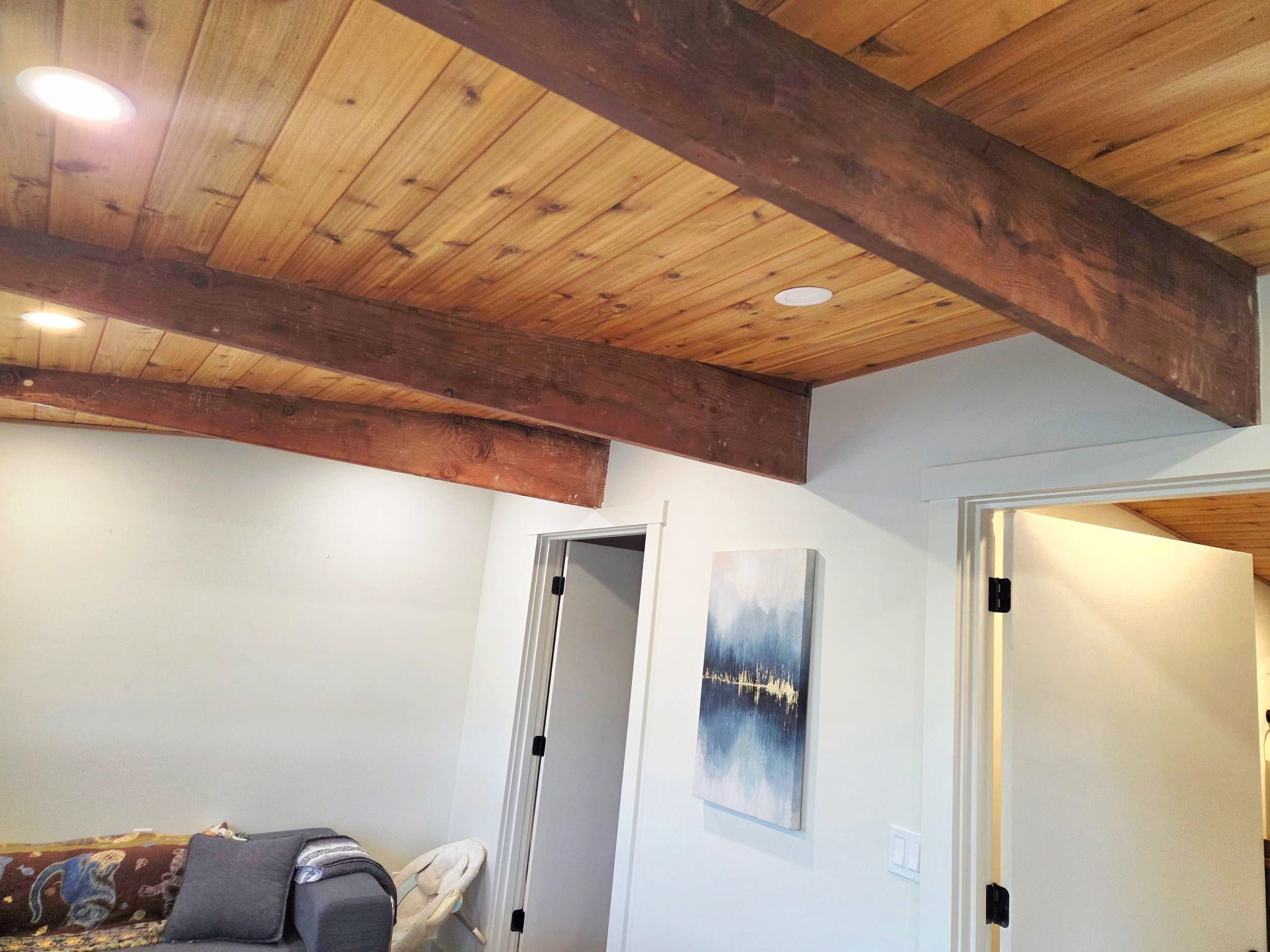 A room with a wooden ceiling, a white door, and a painting on the wall.