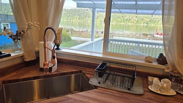 Una cocina con un lavaplatos de acero inoxidable, un escurreplatos y vistas a un lago a través de un ventanal.