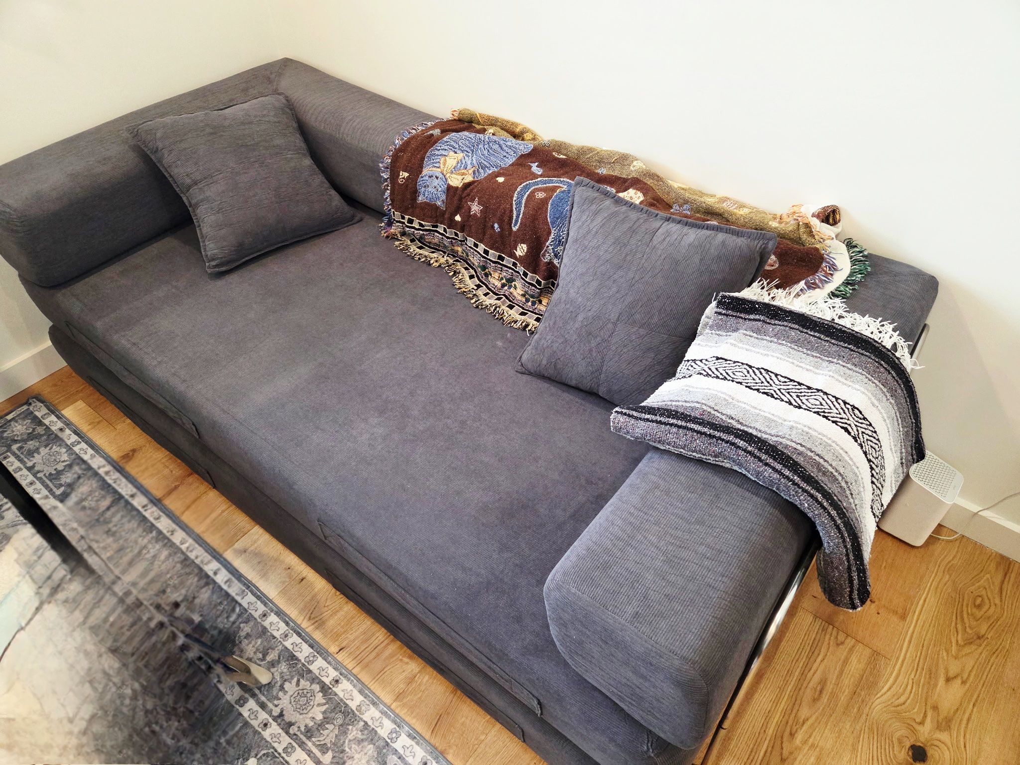 A grey sofa with a patterned throw blanket and a grey pillow.