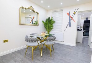 A dining area with a glass table, tufted chairs, a gold-framed mirror, and a plant. - Cosy 3 Bedroom House In Manchester Sleeps 7 (Salford)