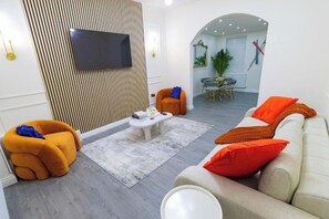 Un salon moderne avec un canapé, un fauteuil et un téléviseur à écran plat fixé au mur.