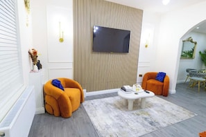 A modern living room with a flat-screen TV, two orange armchairs, a white coffee table, and a patterned rug. - Cosy 3 Bedroom House In Manchester Sleeps 7 (Salford)