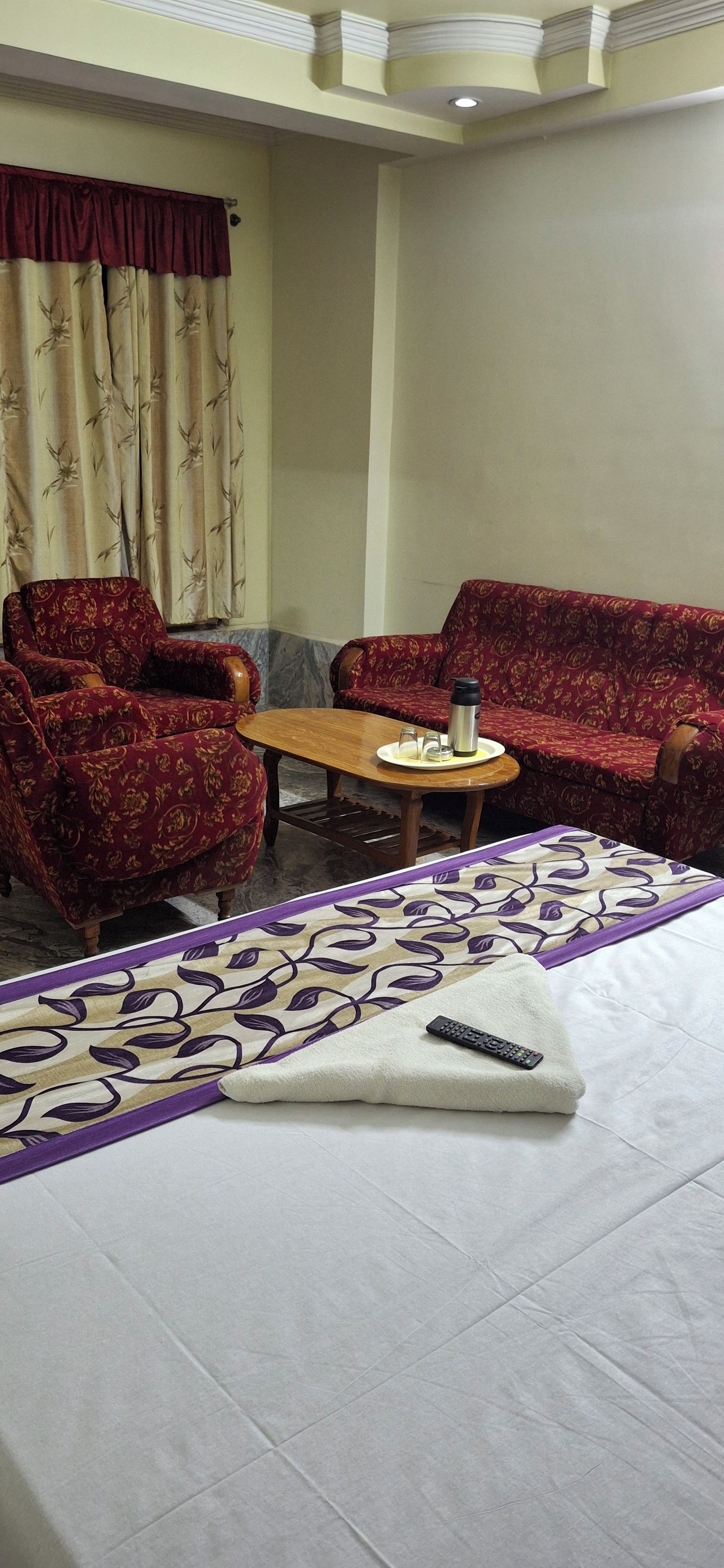 Habitación de hotel con una cama, dos sillones, un sofá, una mesita y un control remoto sobre la cama.