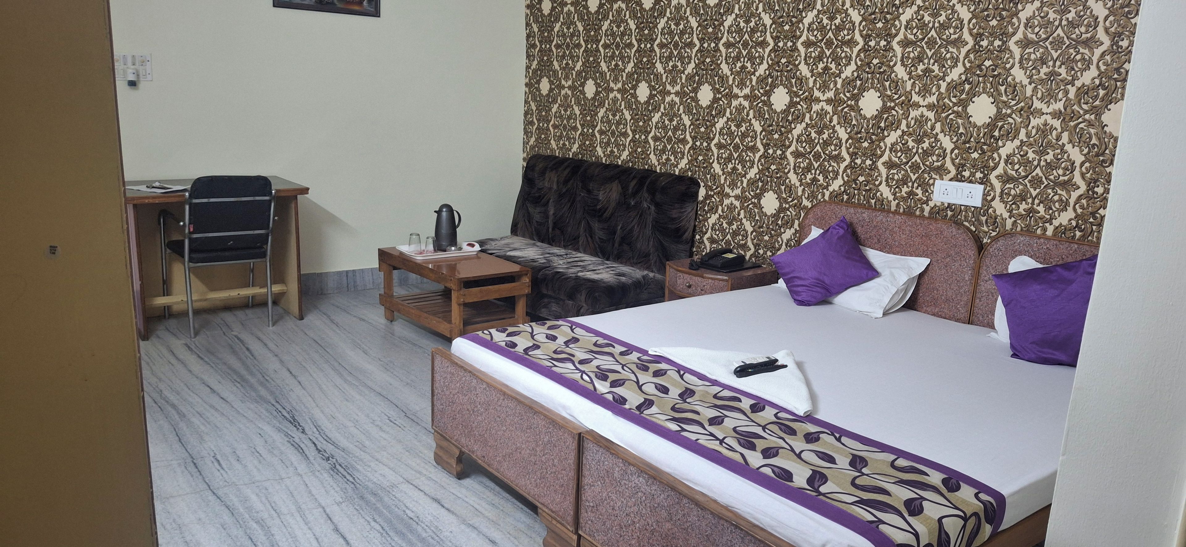 Habitación de hotel con cama, una mesita, una silla, una mesita de noche y papel tapiz estampado.