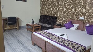Quarto de hotel com cama, mesa pequena, cadeira, mesa de cabeceira e papel de parede estampado.