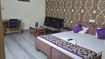 Habitación de hotel con cama, una mesita, una silla, una mesita de noche y papel tapiz estampado.