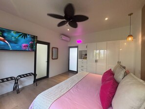 Ein Schlafzimmer mit Bett, Deckenventilator, Fernseher, Kleiderschrank und Spiegel.