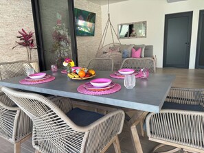 A dining area with a long table, wicker chairs, and a hanging light fixture. - Pool House 311 by Diana (San Juan Cosalá)