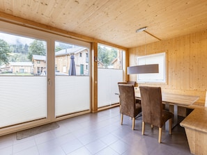Un intérieur moderne avec un plafond en bois, un coin repas comprenant des chaises et une table, et de grandes portes-fenêtres coulissantes donnant sur un espace extérieur.