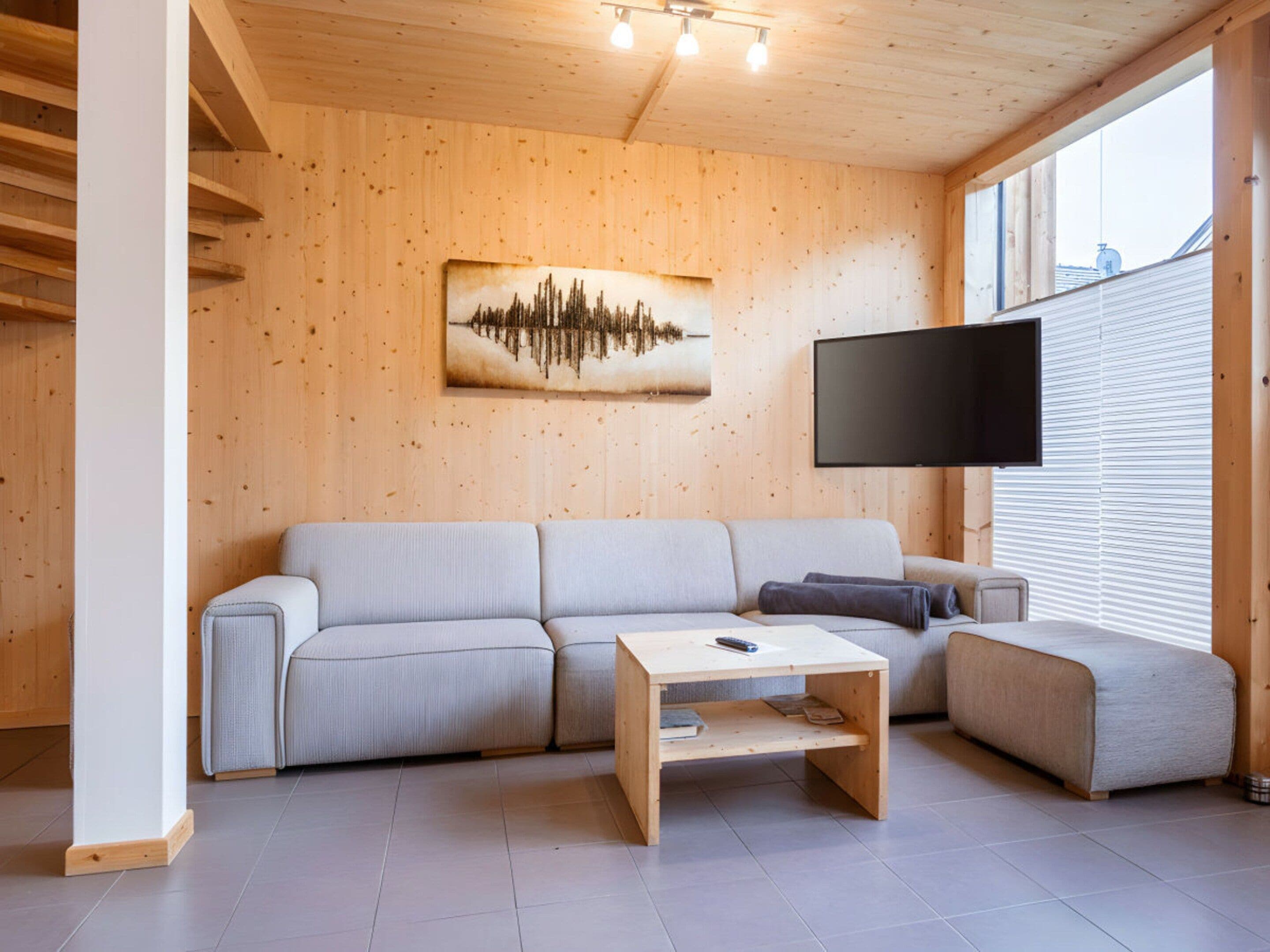 A modern living room with a wooden interior, a sofa, a coffee table, and a flat-screen TV mounted on the wall.