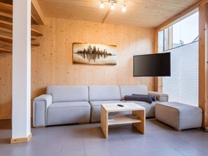 A modern living room with a wooden interior, a sofa, a coffee table, and a flat-screen TV mounted on the wall. - One-bedroom Cabin (Sankt Georgen am Kreischberg)