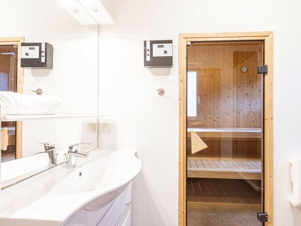 A modern bathroom with a white sink, two mirrors, and a wooden sauna door. - One-bedroom Cabin (Sankt Georgen am Kreischberg)