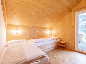 A wooden cabin room with two beds, a small table, and a window with a view of the outside. - One-bedroom Cabin (Sankt Georgen am Kreischberg)