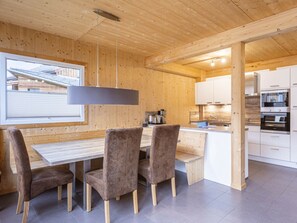 A modern kitchen with wooden cabinetry, a central island, and a dining area with a table and chairs. - One-bedroom Cabin (Sankt Georgen am Kreischberg)