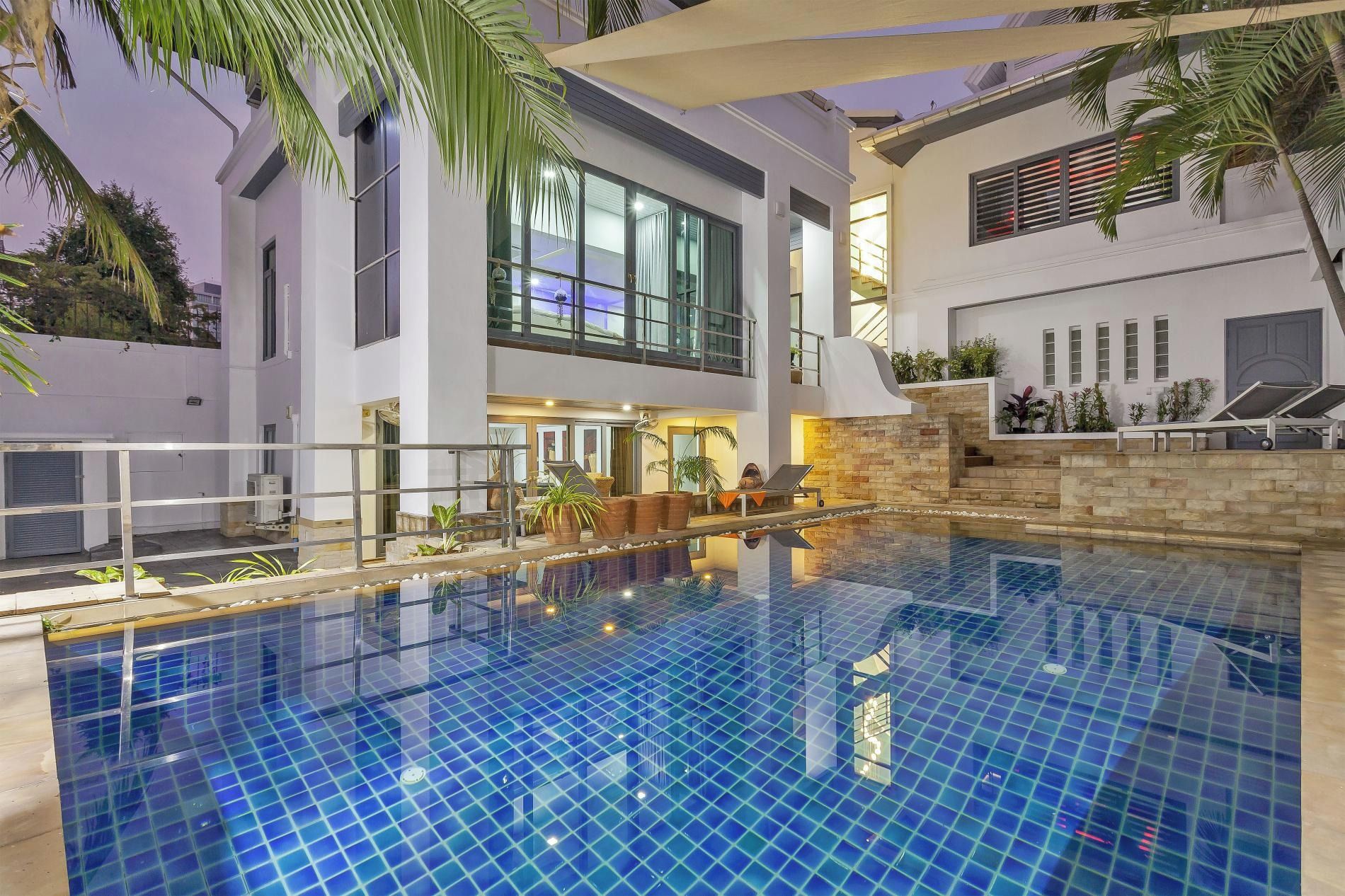 Un bâtiment moderne doté d’une piscine, de grandes fenêtres et d’un espace extérieur aménagé pour s’asseoir.