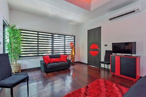 A modern living room with a sofa, a television, a red cabinet, and a large window with blinds. - Pratumnak Hill Pool Villa 4BR (PH1) (Banglamung)