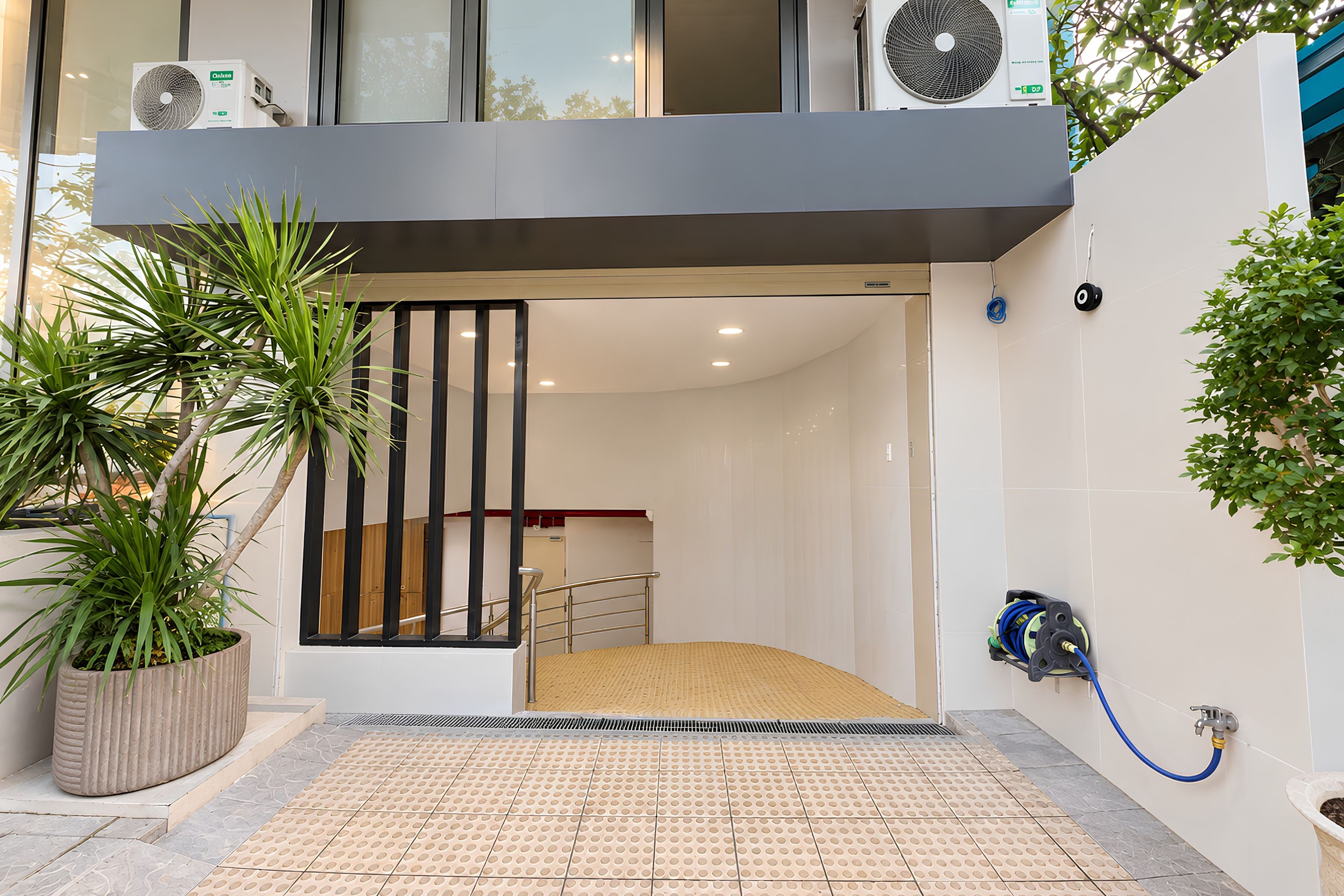 A modern entrance with a ramp, potted plants, and a blue hose on the wall.