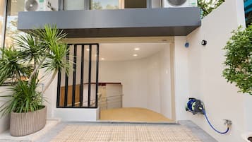 A modern entrance with a ramp, potted plants, and a blue hose on the wall.