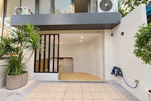 Una entrada moderna con rampa, plantas en macetas y una manguera azul en la pared.