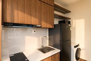 A modern kitchen with wooden cabinets, a built-in oven, a stainless steel sink, and a black refrigerator. - MT Danang Hotel - Near Dragon Bridge (An Hai)