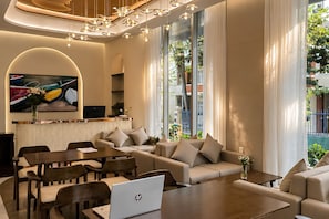Una sala de estar moderna con sofá, mesa de comedor y sillas, una computadora portátil sobre la mesa y un televisor en la pared.
