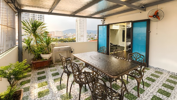 Eine Dachterrasse mit Tisch und Stühlen, Blumentöpfen und Blick auf die Stadtlandschaft.
