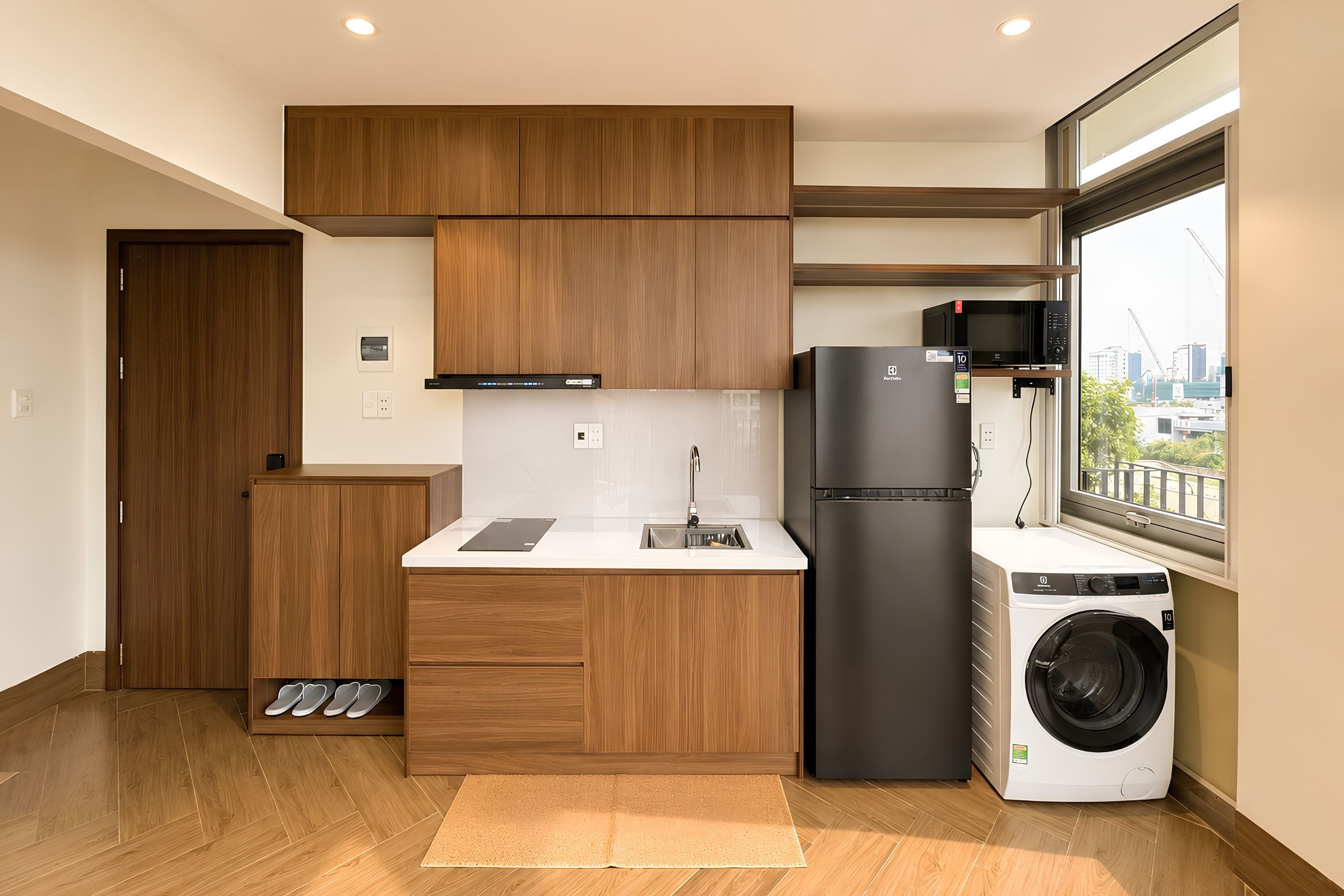 Una cocina compacta con armarios de madera, microondas integrado, refrigerador y lavadora.