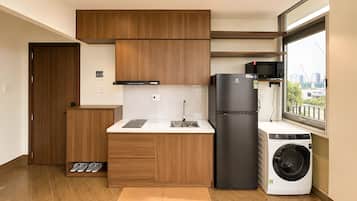 Una cocina compacta con armarios de madera, microondas integrado, refrigerador y lavadora.