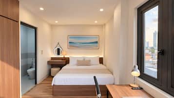Et moderne hotelværelse med seng, sengebord, lampe og et vindue med udsigt over byen.