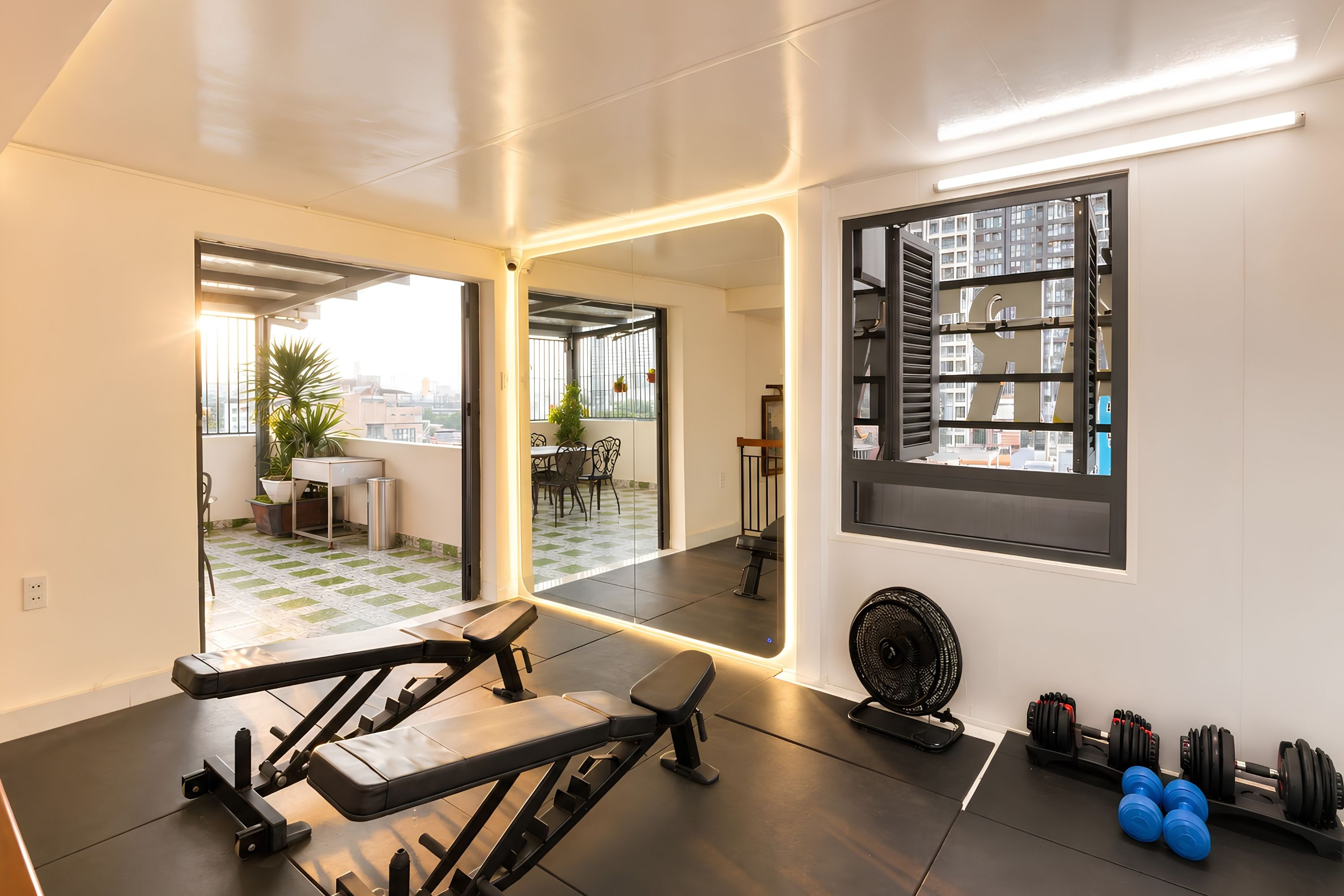 A modern gym with exercise equipment, a large mirror, and a view of the city through a window.