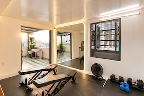 Un gimnasio moderno con equipo de ejercicio, un espejo grande y vistas a la ciudad a través de un ventanal.