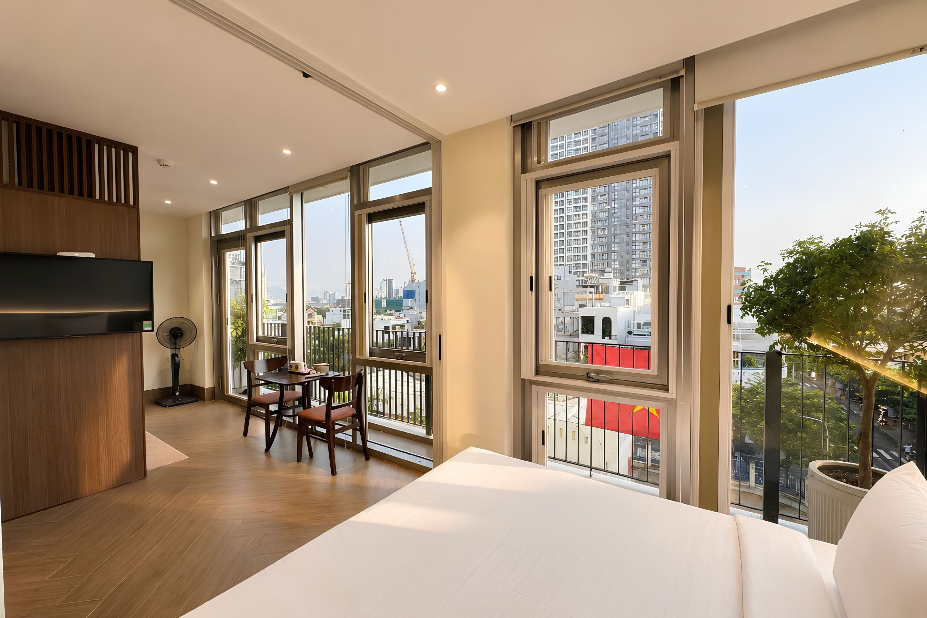 Quarto de hotel moderno com uma cama grande, área de refeições e varanda com vista para a cidade.