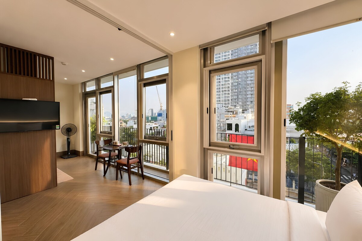 Habitació d'hotel moderna amb un llit gran, zona de menjador i un balcó amb vista a la ciutat.