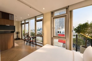 Habitació d'hotel moderna amb un llit gran, zona de menjador i un balcó amb vista a la ciutat.