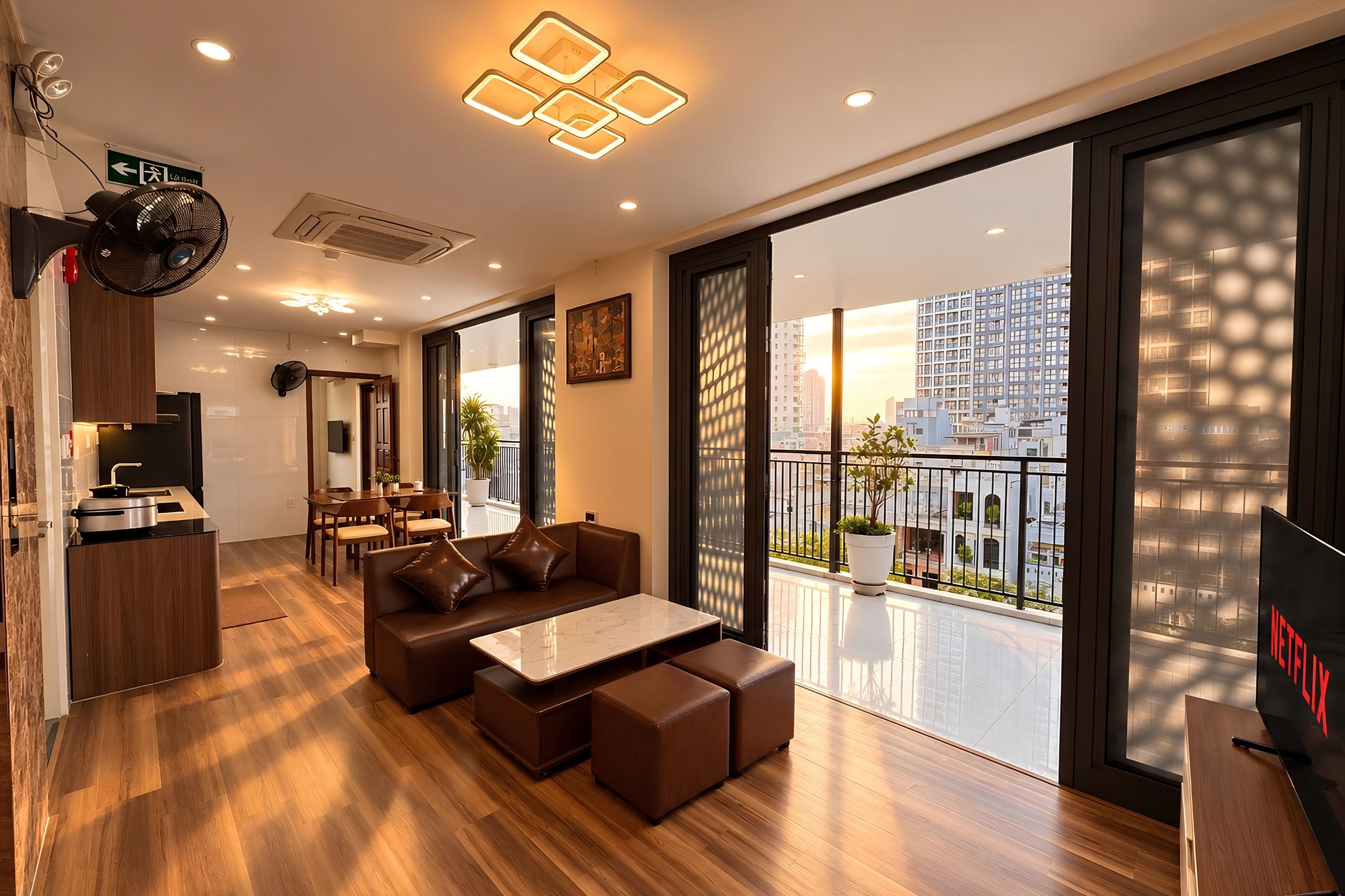 Uma sala de estar moderna com sofá, mesa de centro e área de jantar com cadeiras e mesa. Há uma janela grande com vista para edifícios.